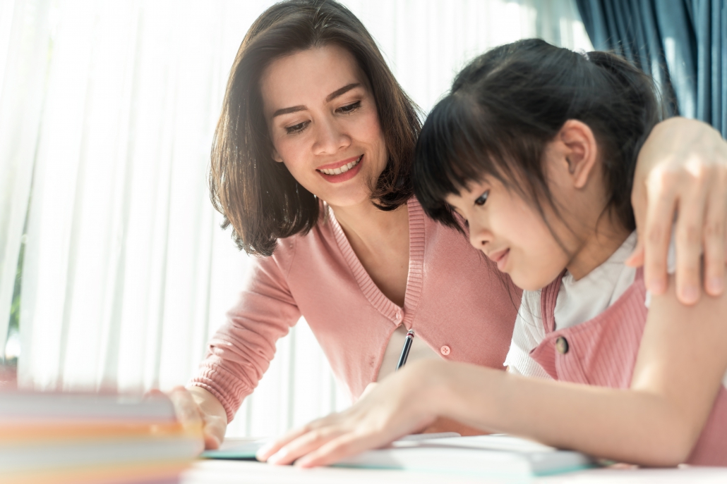 Homeschool Asian young little girl learning, reading and does homework with kind mother help, teach and encourage. Mom hug daughter and smile. Girl happy to study at home education together with mom. Happy mother and daughter homeschool in lockdown